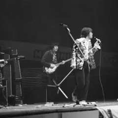 Vier Musiker auf einer Bühne, die alte Rockbands repräsentieren. Einer spielt Schlagzeug, die anderen Gitarre und Bass.