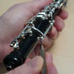 Hände justieren die Mechanik einer Oboe. Ein Schraubenzieher wird angesetzt. Der Weg zum Oboe lernen beginnt oft mit der Pflege des Instruments.