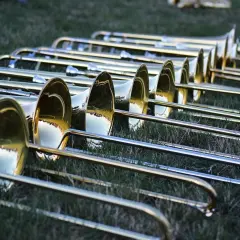 Eine Reihe glänzender Posaunen liegt im Gras. Die Instrumente warten auf ihren Einsatz, vielleicht für ein Konzert oder eine Parade.