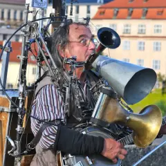 Ein Mann spielt auf einem selbstgebauten Blechblas-Instrument, das mit einem Banjo und vielen mechanischen Teilen verbunden ist.