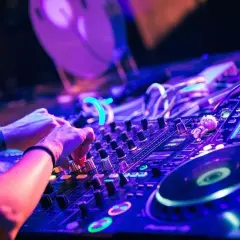 Hände am DJ-Pult, die verschiedene techno subgenres mit Lichtern und Reglern mischen.