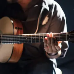 Person übt das Spielen einer akustik gitarre. Hände formen Akkorde auf dem Griffbrett, während die andere Hand die Saiten anschlägt.