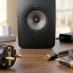 Ein schwarzer KEF-Lautsprecher steht auf einem Holztisch. Kabel und Stecker liegen daneben. Der lautsprecher brummt ohne signal.