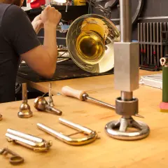 Werkstatt für Blasinstrumente Reparatur: Ein Mann arbeitet an einem glänzenden Horn, Werkzeuge und Mundstücke liegen bereit.