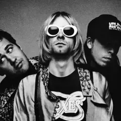 Drei Mitglieder von Grunge-Bands posieren für ein Schwarz-Weiß-Foto. Der Frontmann trägt auffällige weiße Sonnenbrillen.