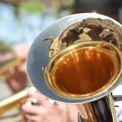 Glänzender Schallbecher einer kleinen Tuba, der eine belebte Straße mit Menschen und Gebäuden widerspiegelt.