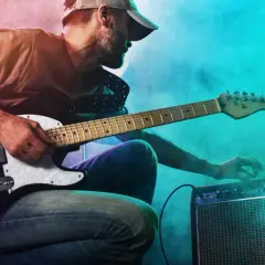 Mann mit Gitarre und Verstärker, der den perfekten gitarren sound einstellt. Nebel und bunte Lichter schaffen eine rockige Atmosphäre.