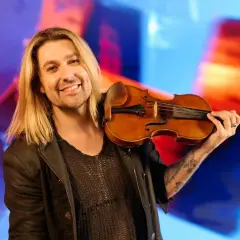Ein lächelnder Mann mit langen blonden Haaren hält eine Geige. Er könnte der beste Geiger der Welt sein, mit seiner Leidenschaft für Musik.