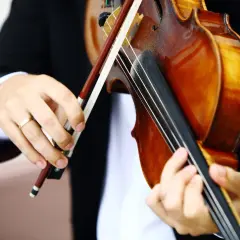 Hände üben das Bratsche lernen. Ein Musiker in schwarzem Sakko hält den Bogen und greift die Saiten der warmbraunen Bratsche.
