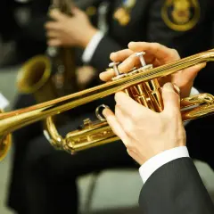 Hände spielen eine glänzende Trompete. Ein Musiker bereitet sich auf sein Referat vor, während im Hintergrund ein Saxophon zu sehen ist.