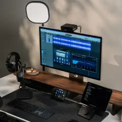 Professionelles Studio-Setup mit Monitor, der Audio-Software anzeigt, Kopfhörern, Mikrofon und Beleuchtung.