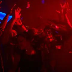 Leute tanzen ausgelassen im Club, die Haare fliegen, Konfetti fällt. Perfekt für eine **2000er Hits playlist**.