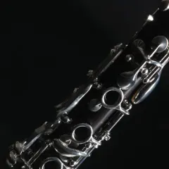 Nahaufnahme eines dunklen Holzblasinstruments, einer Klarinette, mit glänzenden Metallklappen vor schwarzem Hintergrund.