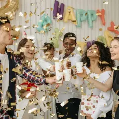 Fröhliche Freunde feiern eine Geburtstagsparty mit Konfetti und Luftballons. Ein "Happy Birthday"-Banner hängt im Hintergrund. Ein tolles Lied für Erwachsene!