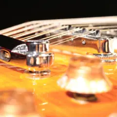 Nahaufnahme einer 12-saitigen Gitarre mit glänzenden Saiten und Chromteilen auf einem orangefarbenen Korpus.