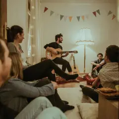 Freunde lauschen gespannt einem Mann mit Gitarre, der gospel songs zum mitsingen anstimmt. Gemütliche Atmosphäre mit bunten Wimpeln.