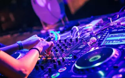 Hände am DJ-Pult, die verschiedene techno subgenres mit Lichtern und Reglern mischen.