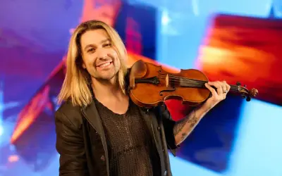 Ein lächelnder Mann mit langen blonden Haaren hält eine Geige. Er könnte der beste Geiger der Welt sein, mit seiner Leidenschaft für Musik.