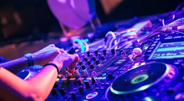 Hände am DJ-Pult, die verschiedene techno subgenres mit Lichtern und Reglern mischen.