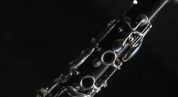 Nahaufnahme eines dunklen Holzblasinstruments, einer Klarinette, mit glänzenden Metallklappen vor schwarzem Hintergrund.