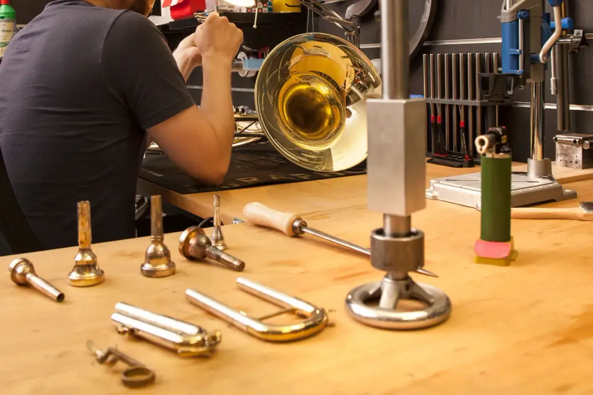 Werkstatt für Blasinstrumente Reparatur: Ein Mann arbeitet an einem glänzenden Horn, Werkzeuge und Mundstücke liegen bereit.