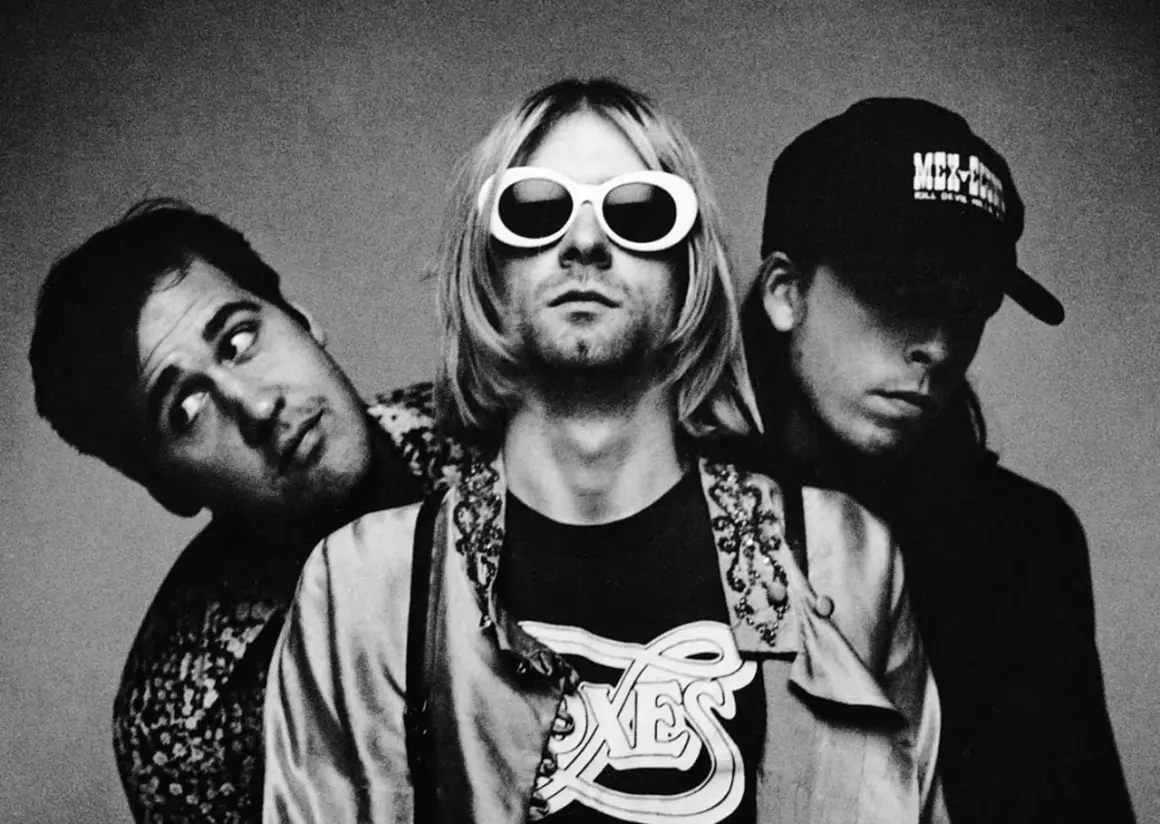 Drei Mitglieder von Grunge-Bands posieren für ein Schwarz-Weiß-Foto. Der Frontmann trägt auffällige weiße Sonnenbrillen.