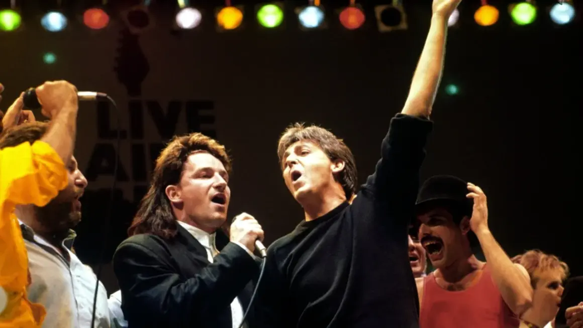 Bono und Paul McCartney singen bei Live Aid. Freddie Mercury jubelt im Hintergrund. Legendäre Live Aid Bands vereint.