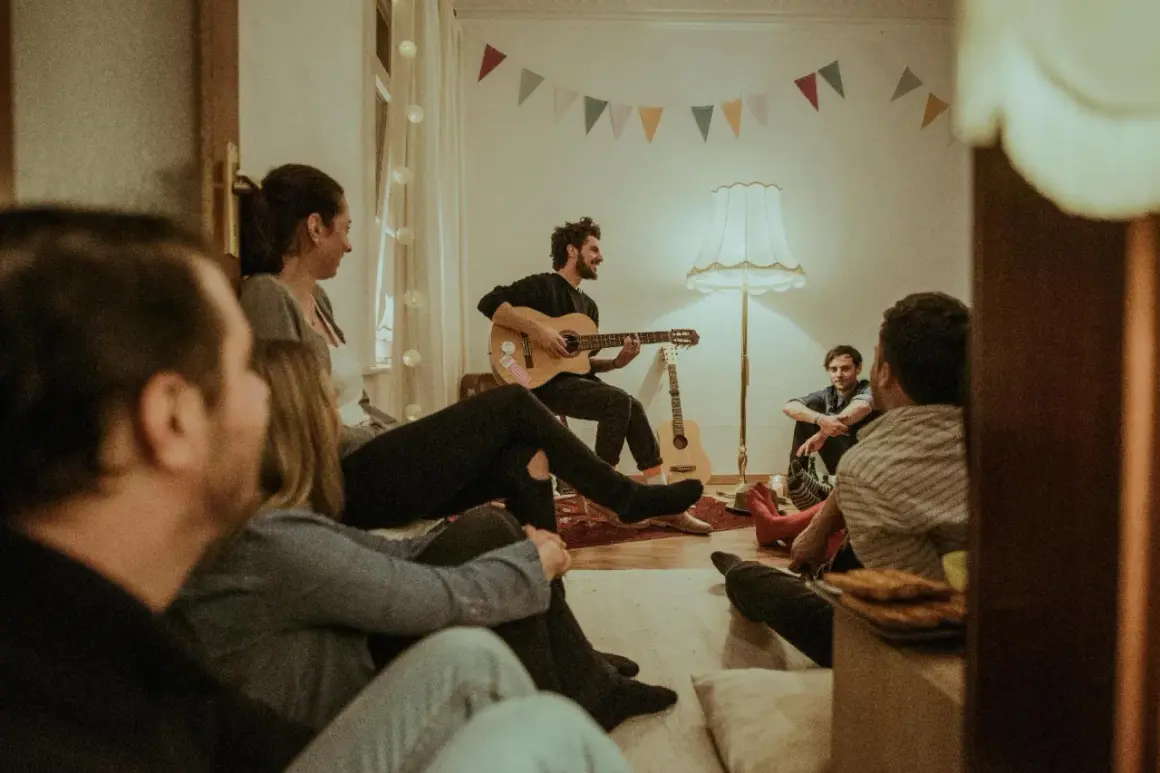 Freunde lauschen gespannt einem Mann mit Gitarre, der gospel songs zum mitsingen anstimmt. Gemütliche Atmosphäre mit bunten Wimpeln.