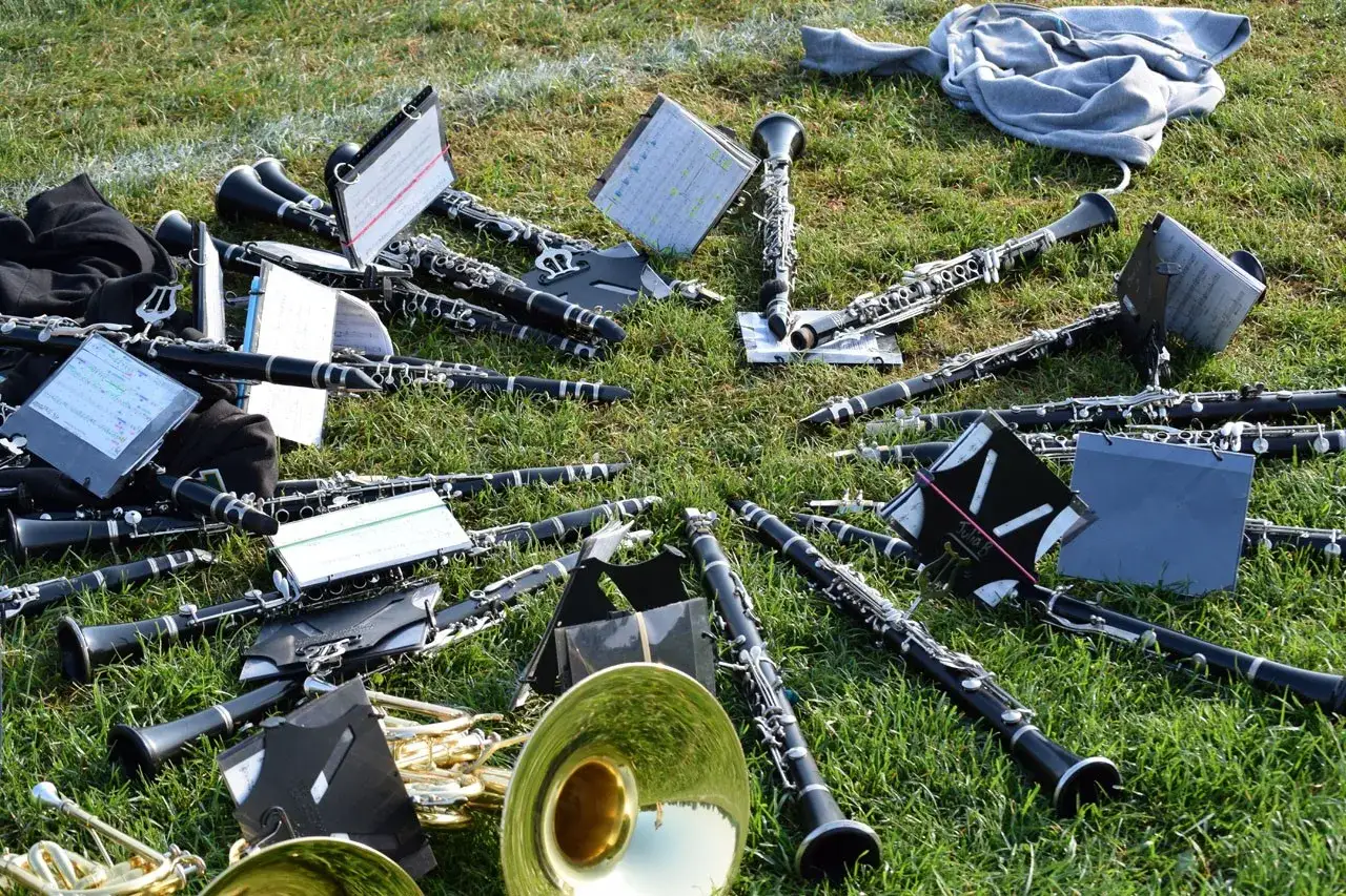Viele Klarinetten und ein tief klingendes Blasinstrument liegen auf dem Gras. Notenbl&auml;tter sind zwischen den Instrumenten verteilt.
