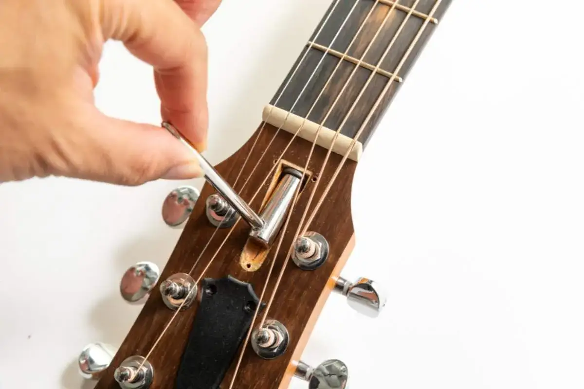 Hand adjusts truss rod on guitar neck.