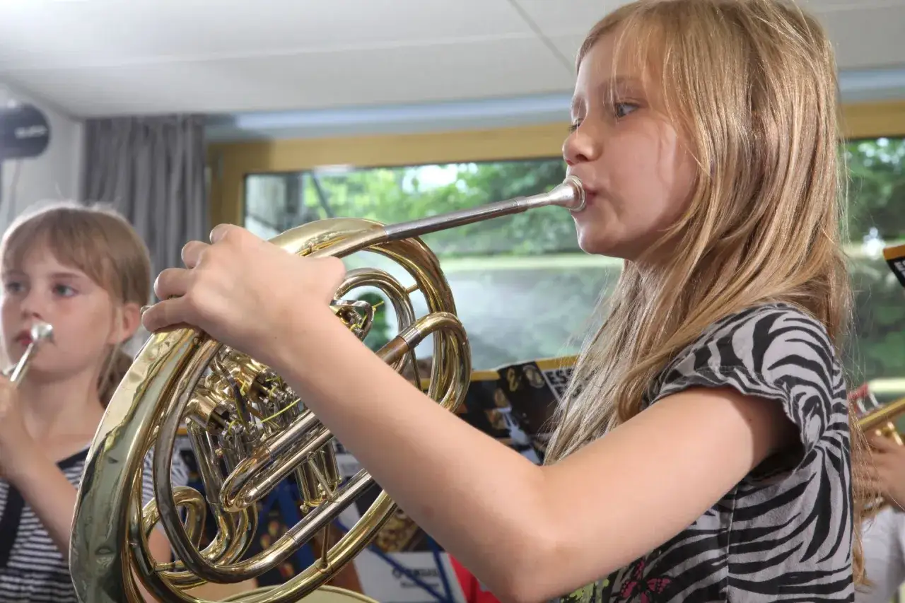 Ein Mädchen übt auf einem Waldhorn, einem der vielen horn instrument arten. Ein anderes Kind spielt im Hintergrund.