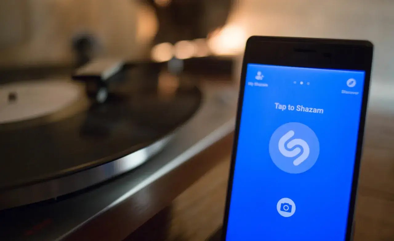 Ein Smartphone mit der Shazam-App, bereit, Musik zu erkennen, steht neben einem Plattenspieler.