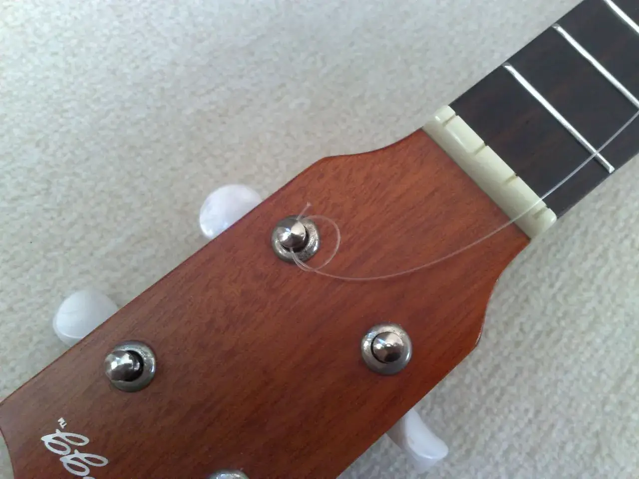 Nahaufnahme des Kopfes einer Ukulele, bereit für den Wechsel der ukulele saiten. Ein Saitenhalter ist sichtbar.