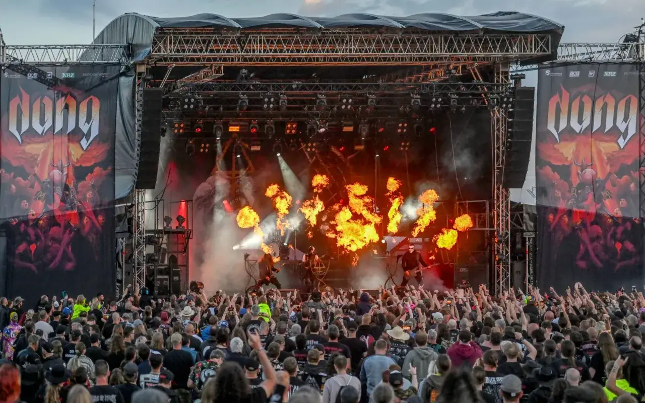 Feuerfont&auml;nen auf der B&uuml;hne, w&auml;hrend eine Band spielt. Die Menge jubelt, viele zeigen die Metal-Geste. Hier sind die metal frauen!