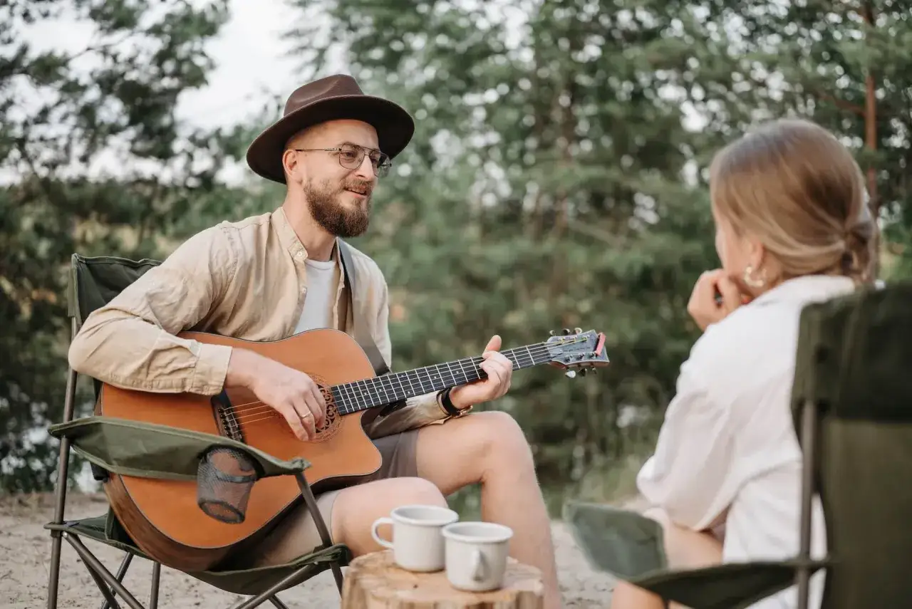 Mann mit Hut spielt Akustikgitarre f&uuml;r Frau im Freien. Vielleicht lernt er gerade, wie man Akustikgitarre lernt und teilt seine Fortschritte.