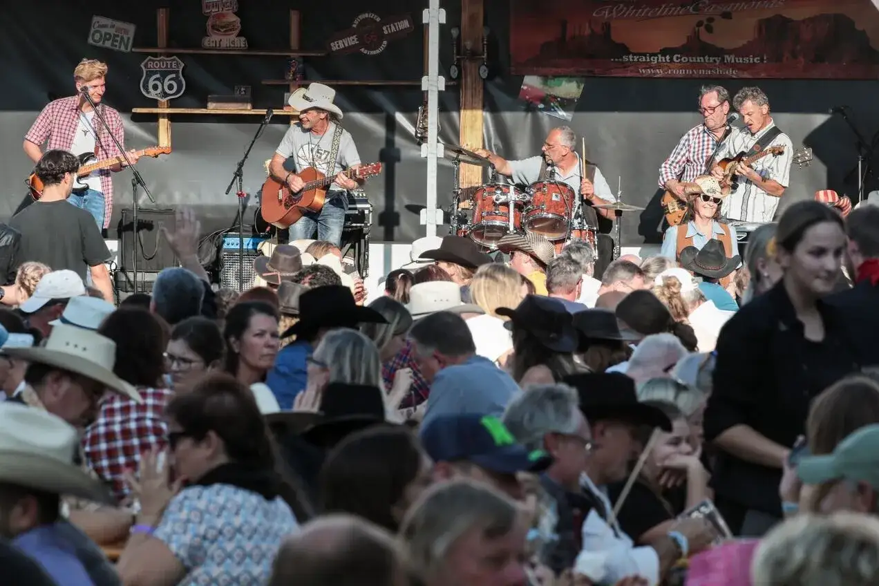Country-Musik-Band spielt auf einer B&uuml;hne, w&auml;hrend ein Publikum mit vielen H&uuml;ten zuh&ouml;rt.