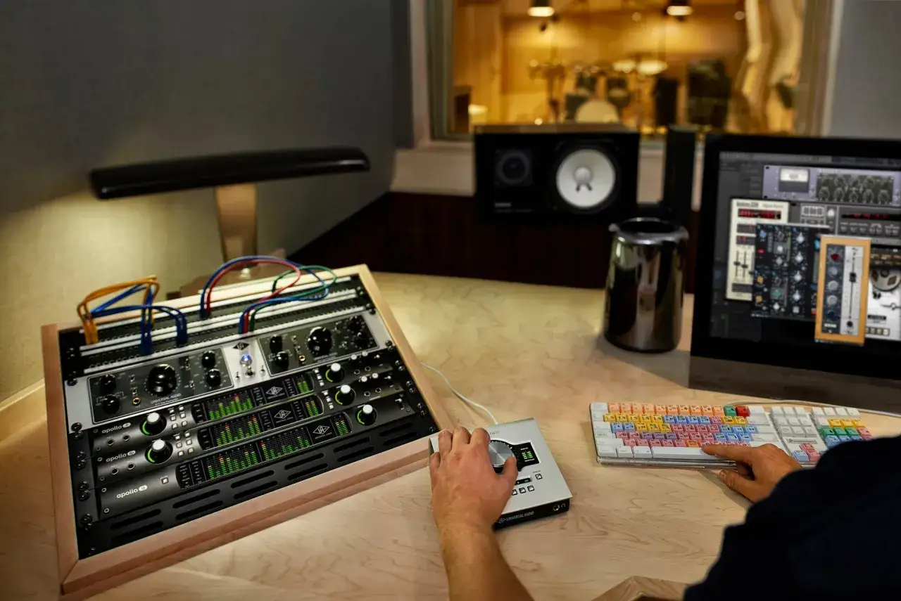 Hand bedient ein Audio-Interface, w&auml;hrend ein midi sequencer auf dem Bildschirm zu sehen ist. Studio-Equipment und ein Schlagzeug im Hintergrund.