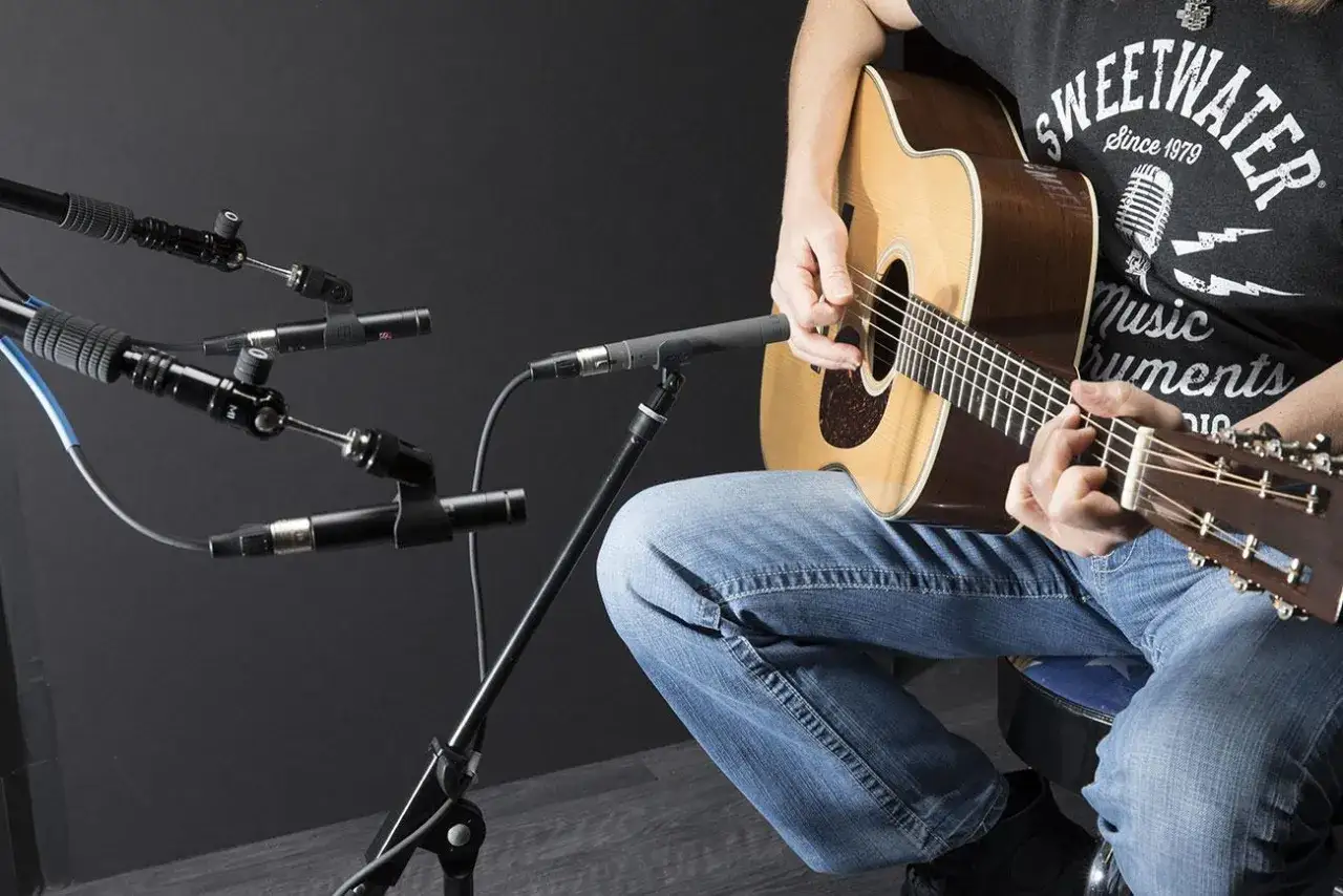 Person spielt Gitarre, während mehrere Mikrofone sie für die Aufnahme positioniert sind.