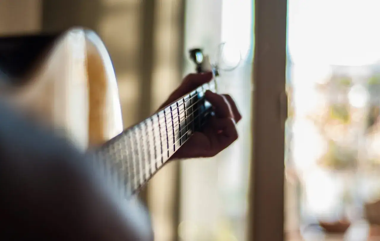 Hand greift nach den Saiten einer Gitarre, um die Oktavreinheit einzustellen. Bokeh-Licht im Hintergrund.