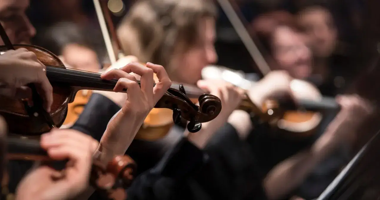 Hände spielen Geigen, während dramatische Musik Klassiker erklingen. Ein Orchester in Aktion.