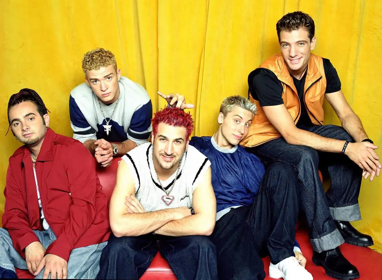 Fünf junge Männer, die die Boybands der 2000er repräsentieren, posieren vor einem gelben Vorhang.