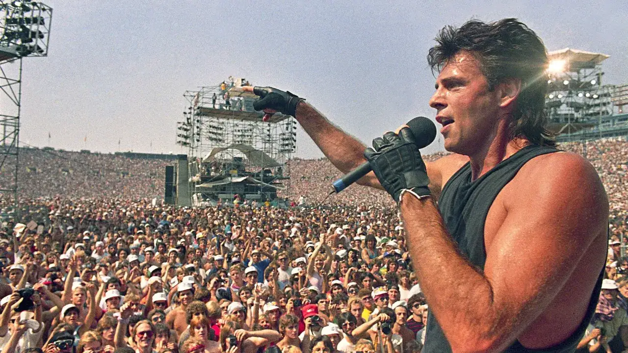 Sänger mit Mikrofon und Handschuhen auf der Bühne vor einer riesigen Menge bei Live Aid. Die Energie der Bands war spürbar.