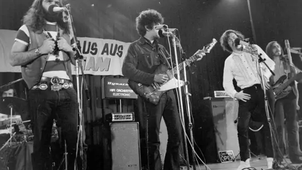 Band auf der Bühne, Gitarrist mit Afro, Sänger mit Schnurrbart, 70er Jahre Rock.