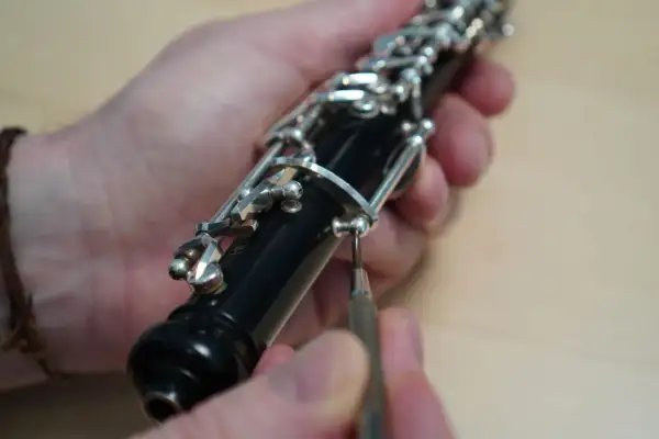 Hände justieren die Mechanik einer Oboe. Ein Schraubenzieher wird angesetzt. Der Weg zum Oboe lernen beginnt oft mit der Pflege des Instruments.