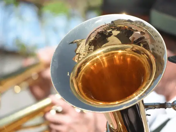 Glänzender Schallbecher einer kleinen Tuba, der eine belebte Straße mit Menschen und Gebäuden widerspiegelt.