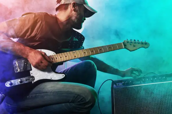 Mann mit Gitarre und Verstärker, der den perfekten gitarren sound einstellt. Nebel und bunte Lichter schaffen eine rockige Atmosphäre.