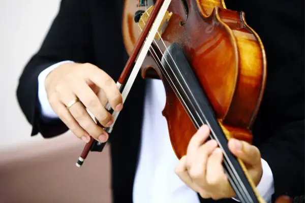 Hände üben das Bratsche lernen. Ein Musiker in schwarzem Sakko hält den Bogen und greift die Saiten der warmbraunen Bratsche.