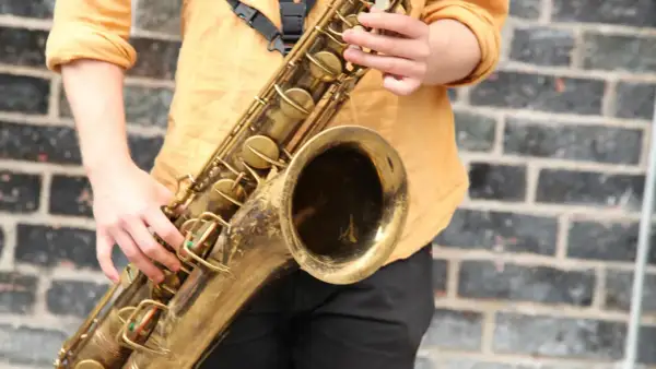 Ein Musiker spielt ein goldenes Saxophon vor einer Ziegelwand. Hier ist ein Saxophon Steckbrief: ein Blasinstrument mit Klappen und einem Mundstück.