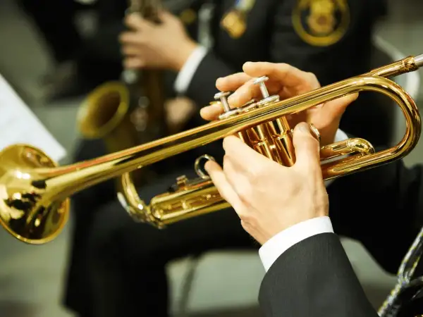 Hände spielen eine glänzende Trompete. Ein Musiker bereitet sich auf sein Referat vor, während im Hintergrund ein Saxophon zu sehen ist.