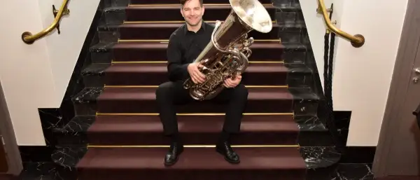 Ein Mann sitzt auf einer Treppe mit einer Tuba. Wer hat die Tuba erfunden? Diese Frage beschäftigt Musiker seit langem.